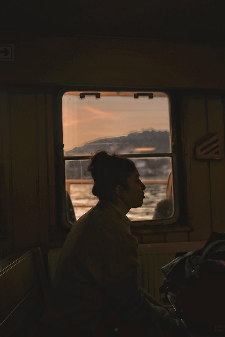 Profile of a woman sitting in a train with a scenic sunset view through the window.