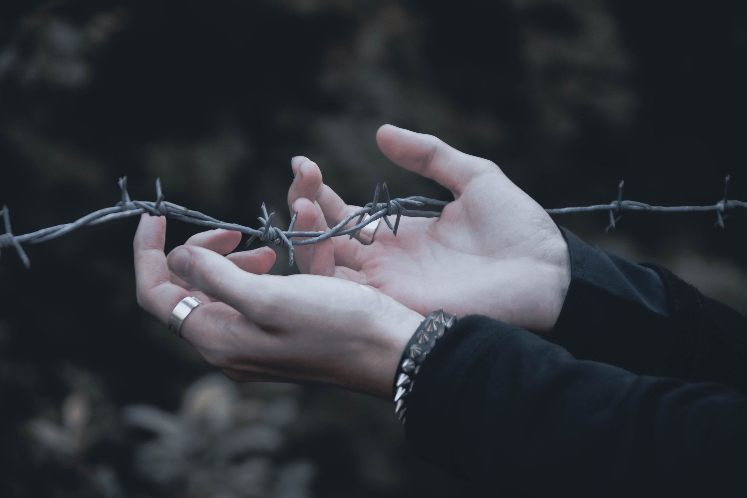 Close-up of hands gently holding barbed wire, emphasizing contrast.